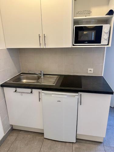 une cuisine avec des armoires blanches, un évier et un micro-ondes dans l'établissement Un studio sympa en centre-ville rue du camas, à Marseille