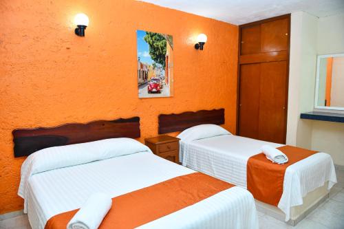 two beds in a room with an orange wall at Hotel Uxulkah in Campeche