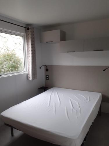 un lit blanc dans une chambre avec une fenêtre dans l'établissement Camping municipal du Moulin Horte sud Aveyron, à Plaisance