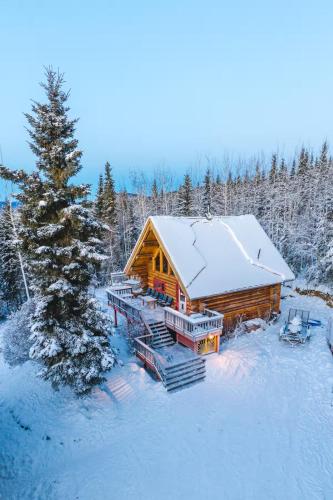 a log cabin with a snow covered roof in the woods at Moose Mountain Cabin- Cozy retreat with aurora views in Fairbanks