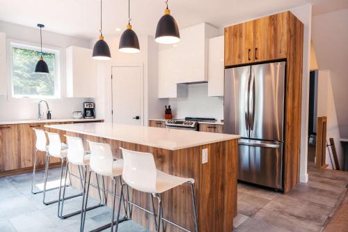 a kitchen with a bar with white chairs and a refrigerator at Le Yéti de Tremblant in La Conception