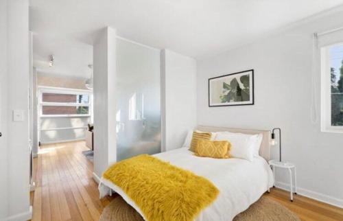 a white bedroom with a bed with a yellow blanket at Great St Kilda location with free parking onsite in Melbourne