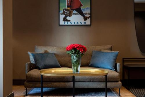 a vase of red flowers on a table in front of a couch at Solo Sokos Hotel Lahden Seurahuone in Lahti