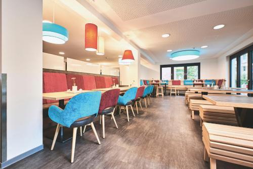 a dining room with tables and chairs and blue chairs at Jugendgästehaus Aasee in Münster