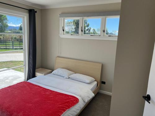 a bedroom with a bed with a red blanket and two windows at Greytown Martinborough mansion in Greytown