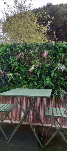 a bench and two chairs in front of a green hedge at Le Parasol in Ars-en-Ré