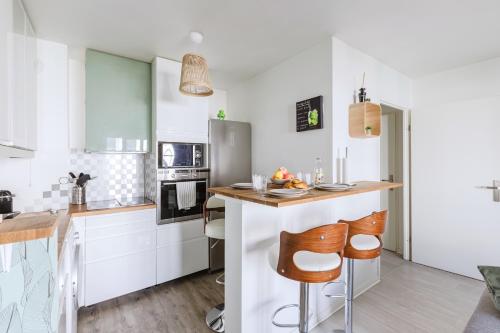 une cuisine avec des placards blancs et un bar avec des tabourets dans l'établissement L'Eden - City Center - DISNEY 8 min, PARIS 28 min - GARE 1 min - PARKING - Free WIFI, à Bussy-Saint-Georges