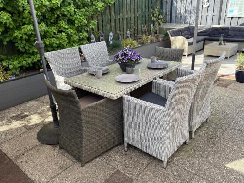 an outdoor table with wicker chairs and a table with flowers at Sunny escape hoek van holland in Hoek van Holland