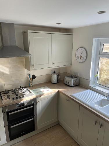 a kitchen with white cabinets and a stove and a sink at Bryntivy - a cheerful stone cottage close to beach in Saint Dogmaels