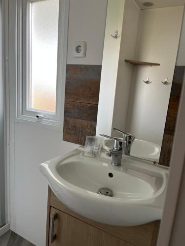 La salle de bains est pourvue d'un lavabo blanc et d'une fenêtre. dans l'établissement Séjour détente en mobil-home 4 à 6 pers Camping 4 étoiles, à Saint-Julien-en-Born