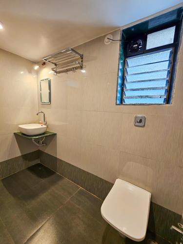 a bathroom with a toilet and a sink and a window at Oxygen Resort, Akshi in Alībāg