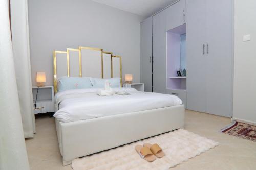 une chambre blanche avec un lit avec des sandales sur le sol dans l'établissement Jay Homes - Rehema Apartments, à Naivasha