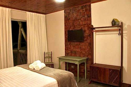 a bedroom with a bed and a table and a television at Pousada Rural Vista do Limoeiro in Itabira