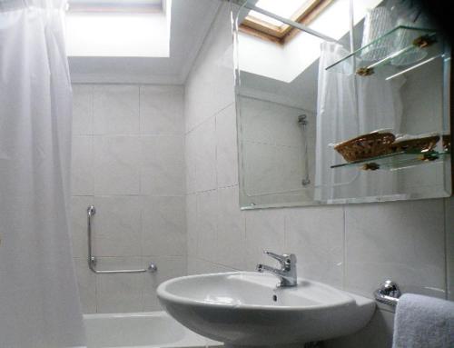Baño blanco con lavabo y espejo en Puente Romano, en Ourense