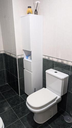 a white toilet in a bathroom with black tiles at Alojamiento La Caridad in La Caridad