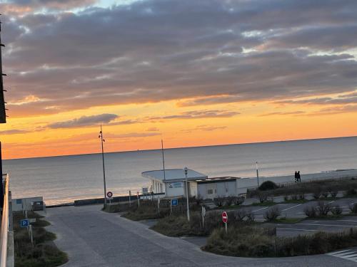 - un coucher de soleil sur une plage avec un bâtiment et l'océan dans l'établissement Appartement vu mer, à Notre-Dame-de-Monts