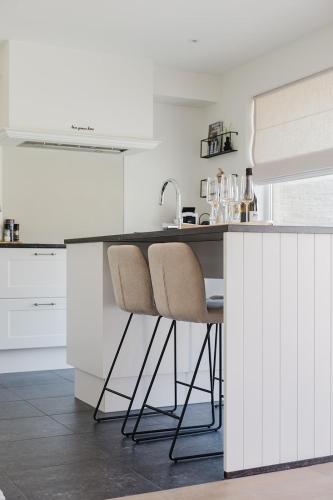 a white kitchen with two chairs at a counter at Casa La Vista - Puur onthaasten met wijds polderzicht in Blankenberge