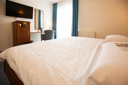 a hotel room with a white bed and a television at Ringhotel Appelbaum Gütersloh in Gütersloh