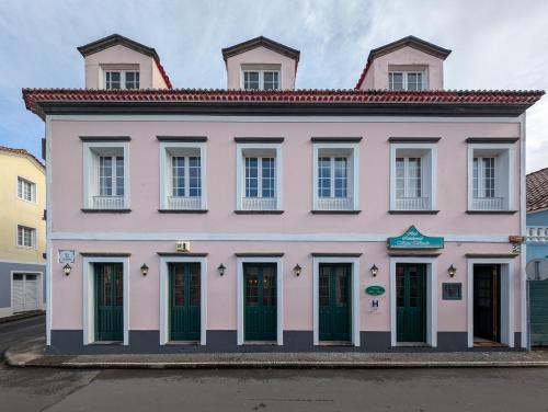 a pink building with green doors on a street at Hotel Vale Verde in Furnas