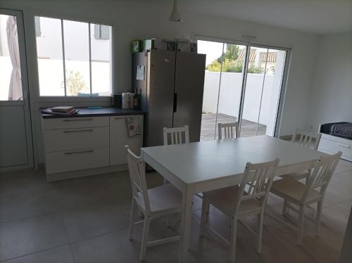 La cuisine est équipée d'une table et de chaises blanches ainsi que d'un réfrigérateur. dans l'établissement Maison RIVEDOUX PLAGE 4 chambres à 300m de la plage - climatisée, à Rivedoux-Plage