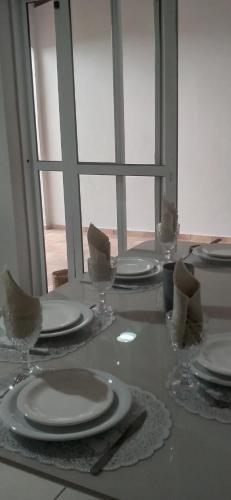 a table with white plates and glasses and a window at Casa das Rosas! Bairro Nobre! Próximo a Basílica Nacional in Aparecida