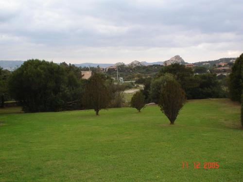 a green field with trees and mountains in the background at Appartamento TARAS in Baja Sardinia