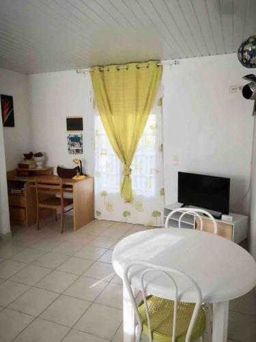a living room with a table and a yellow curtain at La petite Golondrina - Appartement T2 chaleureux dans un cadre paisible verdoyant in Ducos