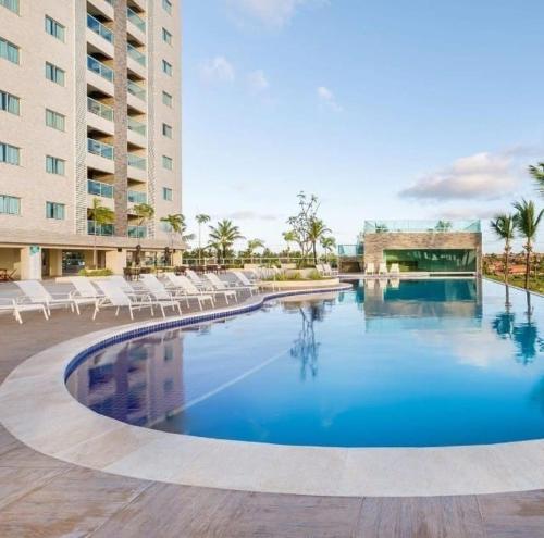a swimming pool with white chairs and a building at Salinas Park Resort in Salinópolis