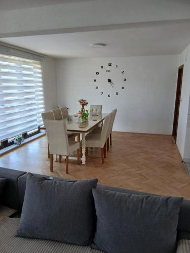 a dining room with a table and chairs and a clock on the wall at Nani Apartman - Banja Ždrelo in Malo Laole