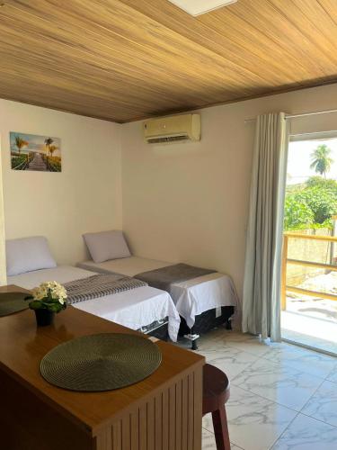 una camera da letto con due letti, un tavolo e una finestra di Flats Rota dos Corais a São Miguel dos Milagres