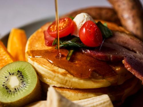 a plate of pancakes with bacon and tomatoes and kiwis at THE LIVELY TOKYO AZABUJUBAN in Tokyo