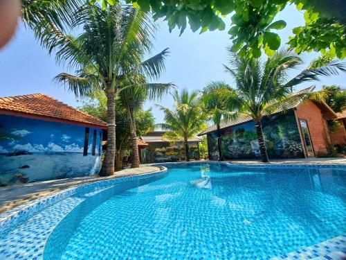 a swimming pool with palm trees next to a building at Xanh Homestay in Phù Cát