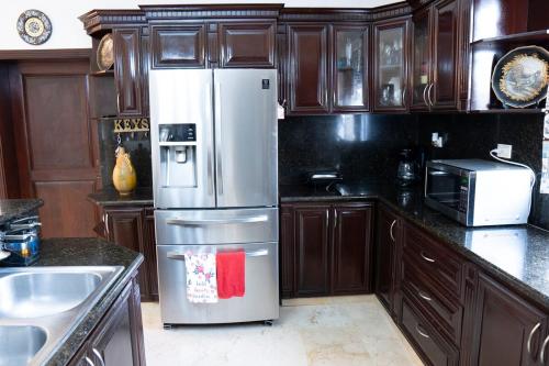 a kitchen with wooden cabinets and a stainless steel refrigerator at Villa La Dueña - Vista Hermosa Luxury Retreat, 5BR Villa with Pool, Swim-Up Bar, Jacuzzi, Chef's Kitchen, Fast Wi-Fi, Full AC, EV Charger and Solar Power, Ideal for Families & Groups in Cancino