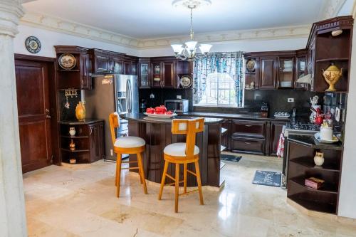 a kitchen with wooden cabinets and a island with bar stools at Villa La Dueña - Vista Hermosa Luxury Retreat, 5BR Villa with Pool, Swim-Up Bar, Jacuzzi, Chef's Kitchen, Fast Wi-Fi, Full AC, EV Charger and Solar Power, Ideal for Families & Groups in Cancino