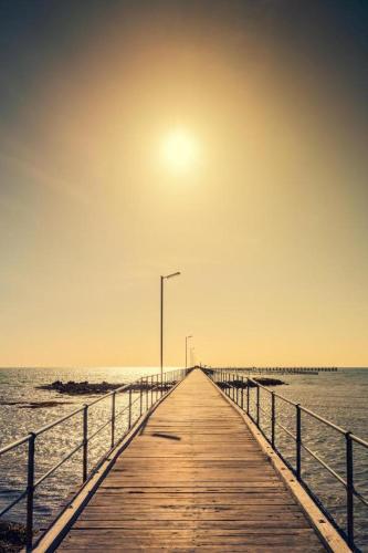 a wooden pier leading to the ocean with the sun in the sky at The Coastal Crab, Moonta Bay in Port Moonta