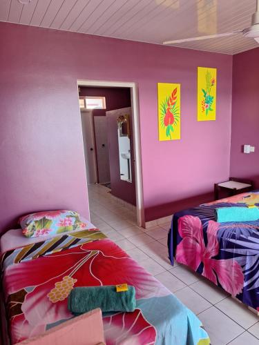 a room with two beds and a pink wall at Pension Tautiare Village in Maupiti