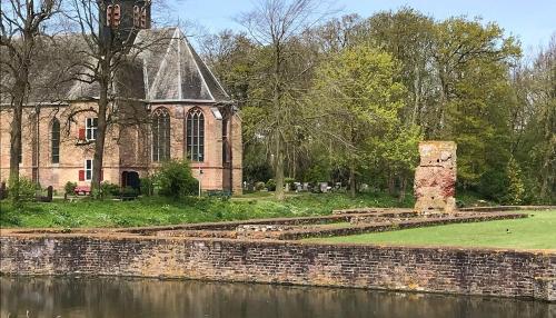 an old building with a clock tower next to a body of water at Slotje in Egmond aan den Hoef