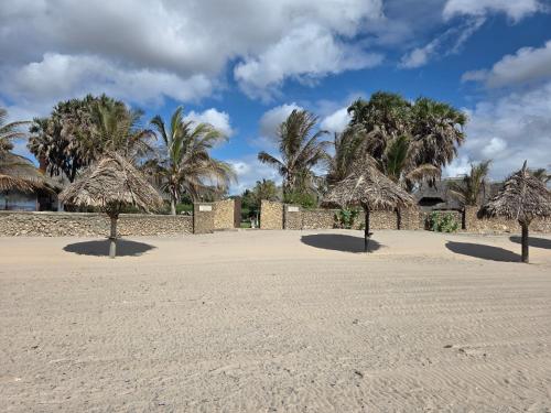 a beach with some straw umbrellas and palm trees at Karibuni, Villa 107, Beachfront Stay with Restaurant, Pool & Bar in Malindi