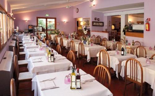 une salle à manger avec des tables blanches et des chaises en bois dans l'établissement Albergo Rossella, à Castiglione della Pescaia