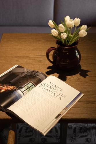a table with a vase of white flowers and a book at Vinte-Quinta da Boavista in Ponte de Lima