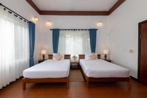 two beds in a room with blue curtains at Atoh's Maison in Siem Reap