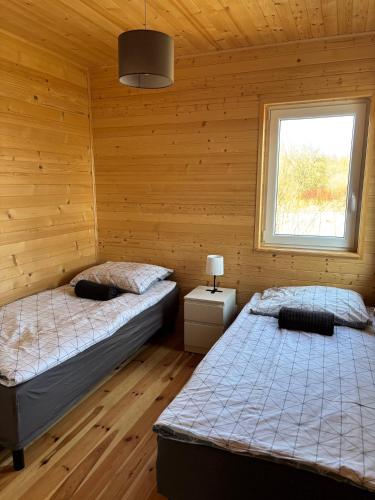 two beds in a room with wooden walls and a window at Domki letniskowe in Ostrów Warcki