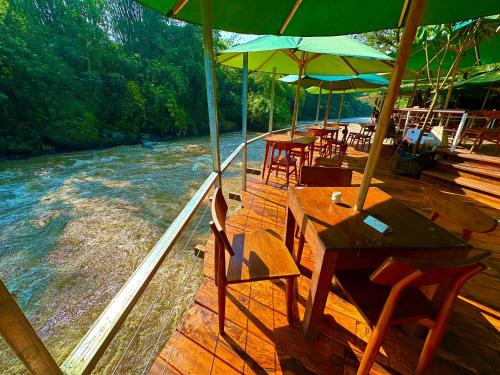 a wooden deck with tables and chairs next to a river at Puunee Wild River Villa's Borobudur in Borobudur