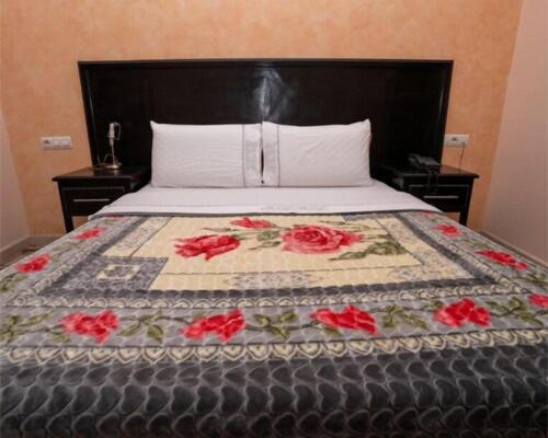 a bed with a quilt with red roses on it at Hotel OUM EL FADL in Fkih Ben Salah