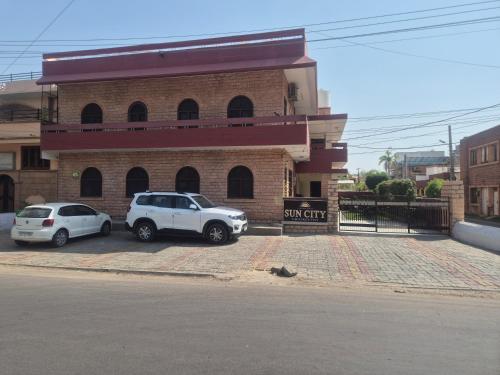 two cars parked in a parking lot in front of a building at Hotel Gajender Niwas Sun City A Boutique Stay in Jodhpur