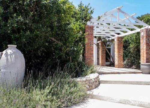 a garden with a white pergola and a brick building at Seeplaas Guesthouse in Groot Brak Rivier