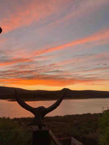 a sunset over a lake with a bird statue at Clanwilliam Dam House in Clanwilliam