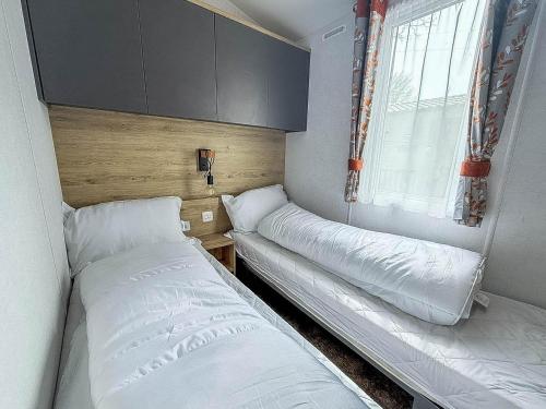 a small bedroom with two beds and a window at Beautiful Caravan With Decking At Azure Seas In Suffolk, Sleeps 6 Ref 32004Az in Lowestoft