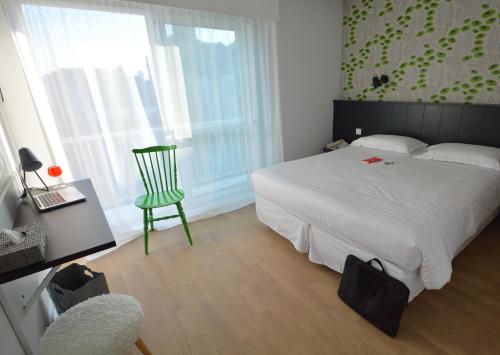 a bedroom with a white bed and a green chair at Logis Hotel Du Port in Plobannalec-Lesconil