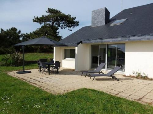 un patio avec une table, des chaises et un parasol dans l'établissement Maison vue mer 8 personnes - Finistère Sud, à Moëlan-sur-Mer
